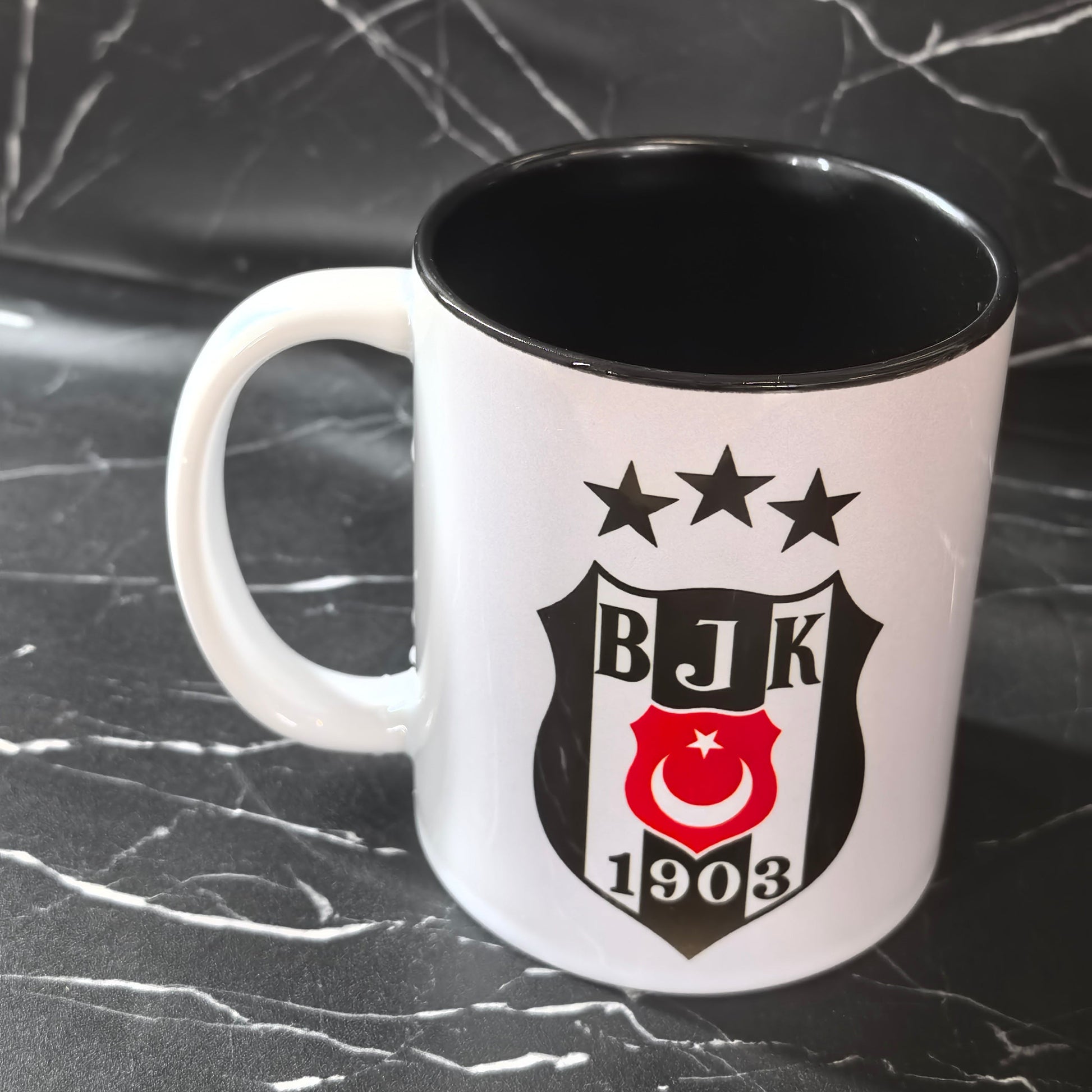 BJK 1903 Fan Tasse mit schwarz-weißem Wappen auf schwarzem Marmor-Hintergrund.