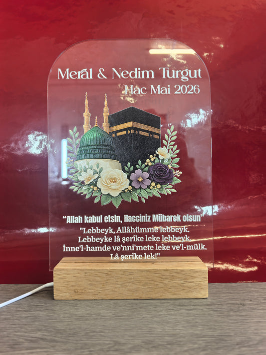 Personalisiertes Hac Acrylglas mit LED-Holzsockel, Kaaba und Moschee-Motiv mit Blumendekoration, gravierte Namen Meral & Nedim Turgut, Hac Mai 2026 und Talbiyya-Gebet, roter Hintergrund