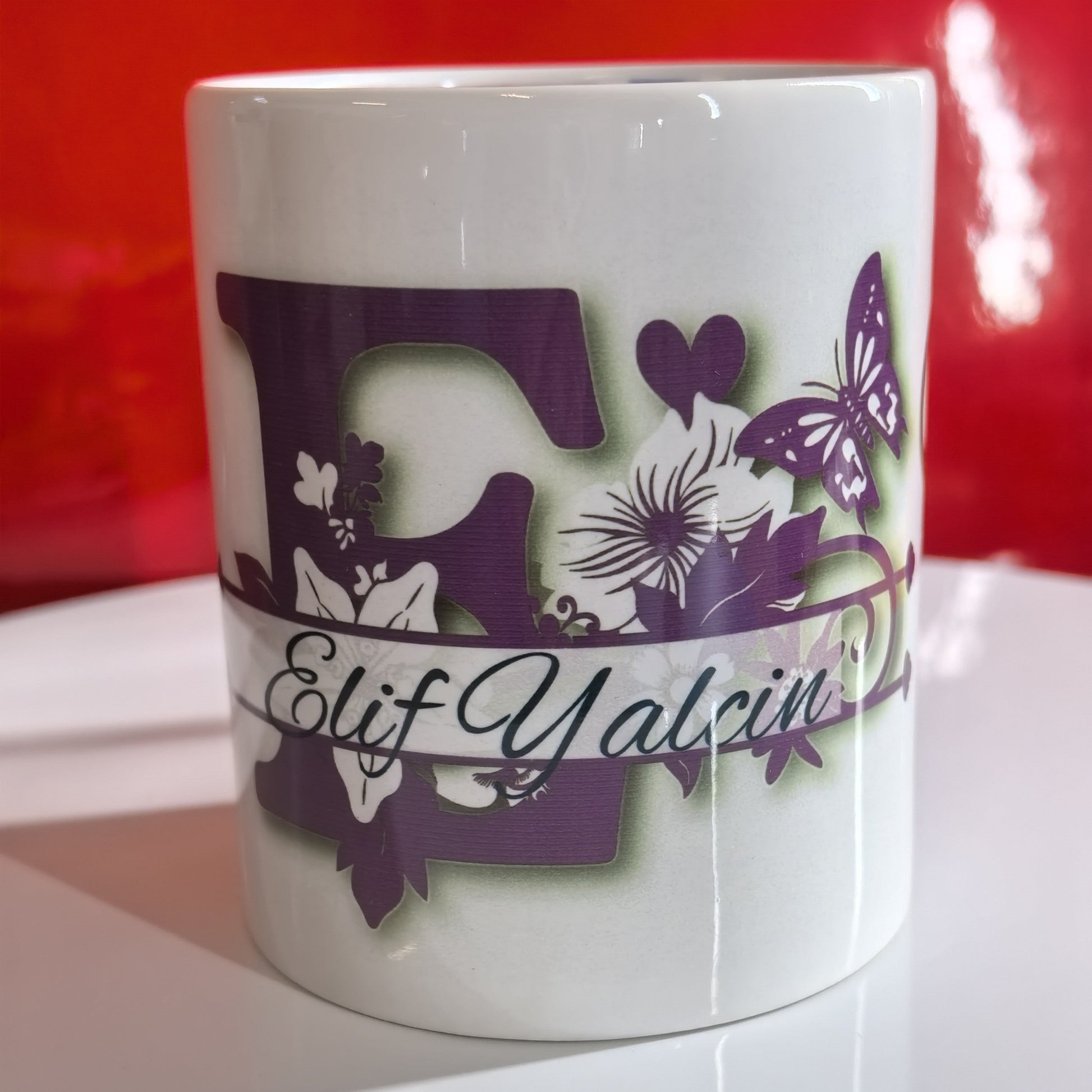 Personalisierte Tasse Anfangsbuchstabe E mit Namen Elif Yalcin und floralen Motiven.