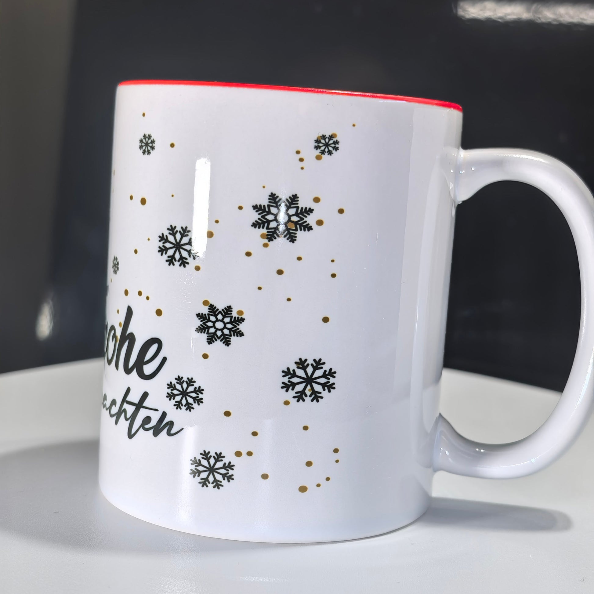 Seite der Weihnachtstasse mit goldenen und schwarzen Schneeflocken und rotem Rand.